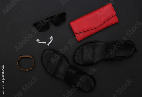 Gadgets and women's accessories on a black background. Sandals, smartphone, headphones, sunglasses, smart bracelet and wallet. Top view. Flat lay