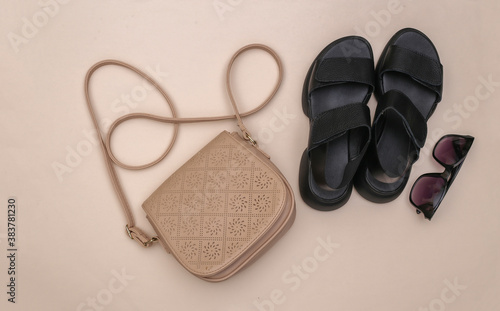 Women's leather sandals, sunglasses and bag on beige background. Women's accessories. Top view. Flat lay