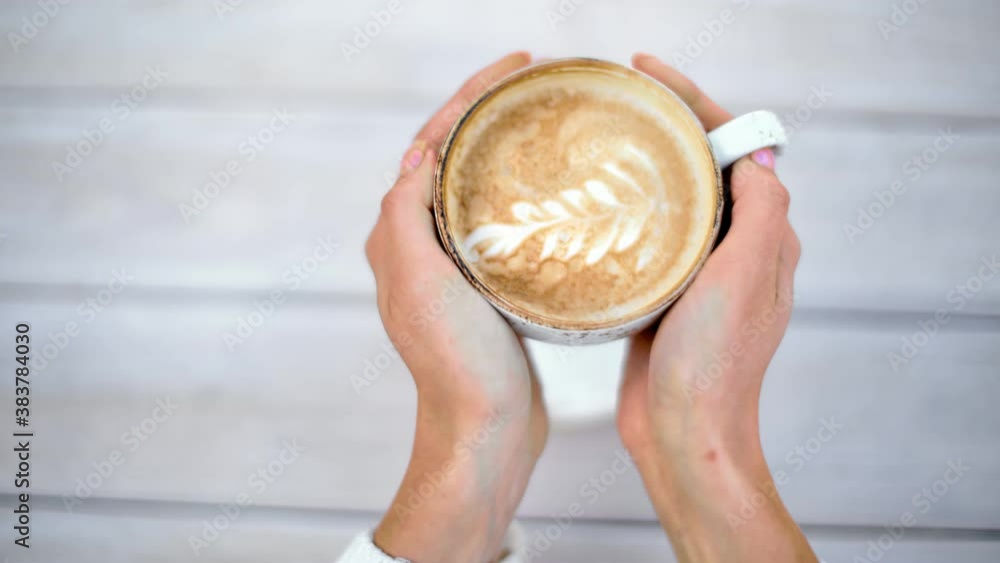 Female hands taking cup of hot cappuccino with latte art from table. Close up shot on 4k RED camera Female hands taking cup of hot cappuccino with latte art from table. Close up shot on 4k RED camera