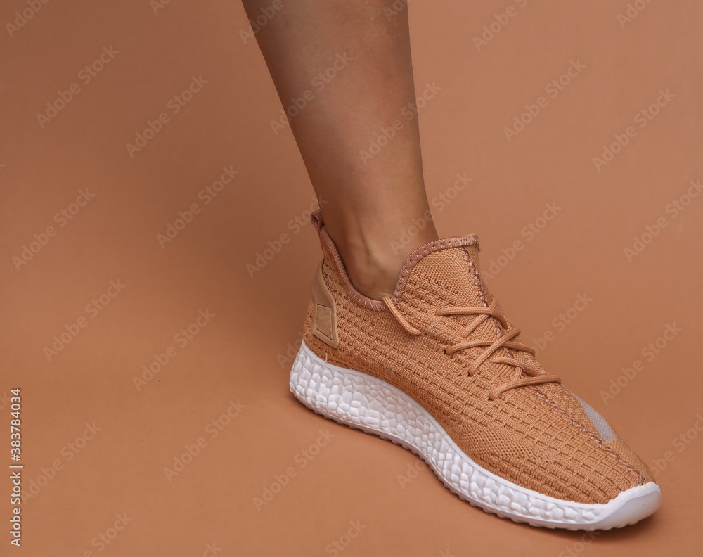 Female feet in trendy sports shoes on brown background