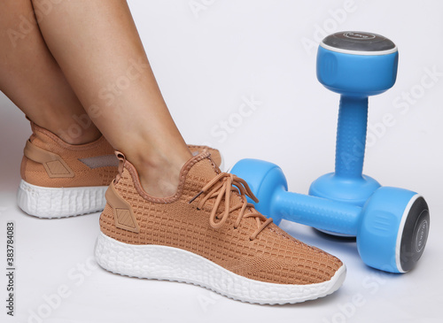 Female legs in trendy sports shoes and dumbbells on a white background. Sport concept