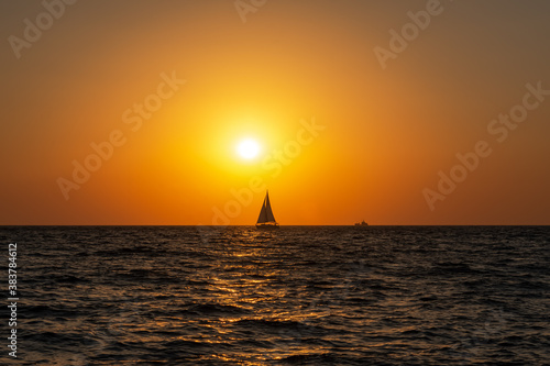 A lone sailboat at sunset. Atmospheric seascape with orange sun. Cloudless sky. The concept of relaxation and relaxation. Idyll. Sea with a little excitement. Sailboat out of focus.