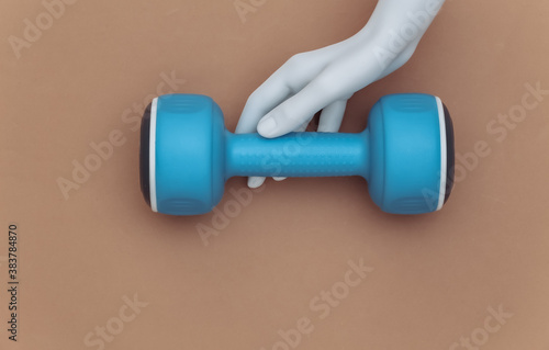 White mannequin hand holds plastic dumbbells on brown background. Sport and fitness concept