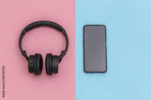 Wireless stereo headphones and smartphone on pink blue pastel background. Top view