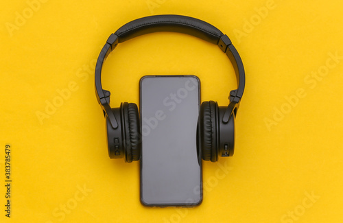 Smartphone with wireless stereo headphones on yellow background. Top view