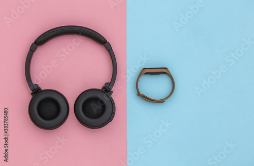 Wireless stereo headphones and smart bracelet on pink blue pastel background. Modern gadgets. Top view