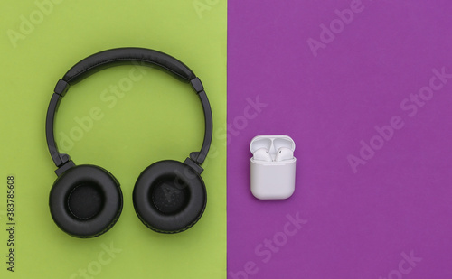Wireless large stereo headphones and small earbuds with charger case on purple green background. Top view