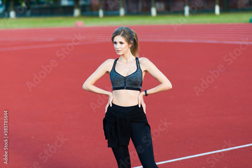 A female coach with dark hair stands on the red running track of the stadium