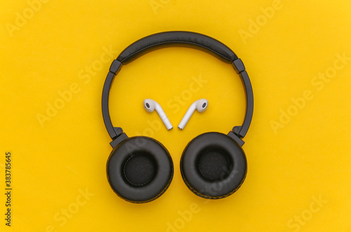 Wireless large stereo headphones and small earbuds on yellow background. Top view