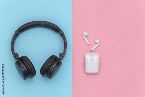 Wireless large stereo headphones and small earbuds with charger case on pink blue pastel background. Top view