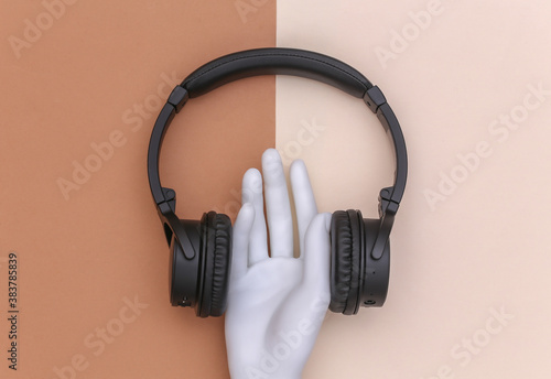 Mannequin hand with stereo headphones on brown beige background. Minimalism concept art. Top view