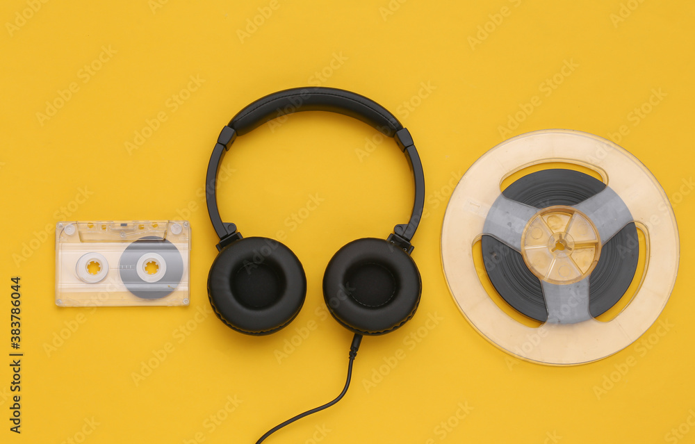 Stereo headphones and magnetic audio reel, audio cassette on yellow background. Top view. Flat lay Stereo headphones and magnetic audio reel, audio cassette on yellow background. Top view. Flat lay