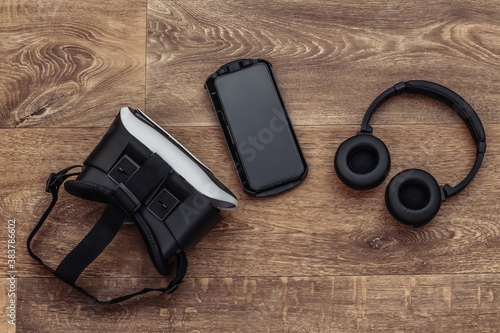 Flat lay composition of modern gadgets. Vr helmet, headphones and smartphone on wooden background. Top view