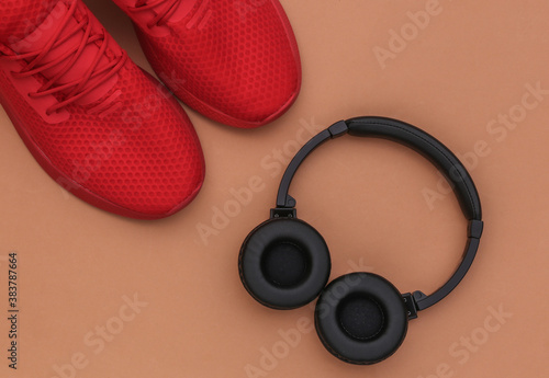Sports shoes with stereo headphones on brown background. Top view