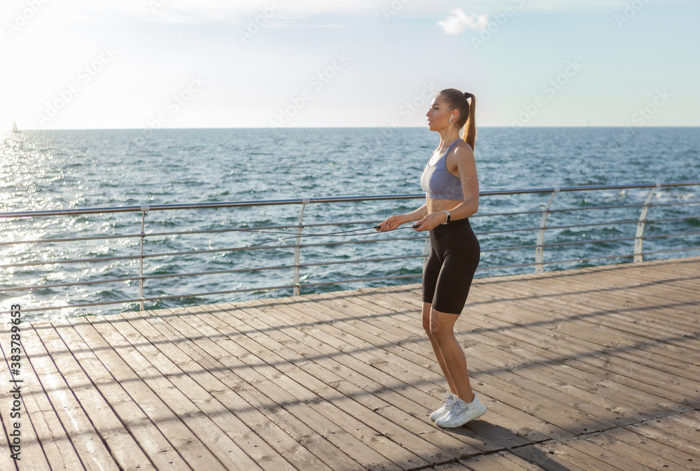 Fit woman jumping rope on the beach at sunrise