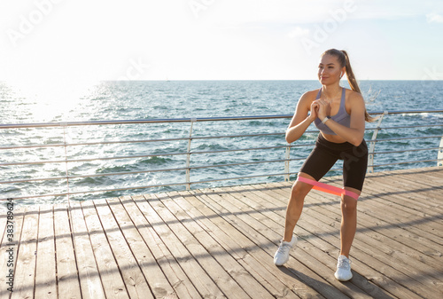 Slim fit woman in sportswear exercises with fitness rubber bands on the beach at sunrise © splitov27