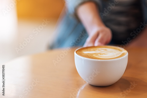 Closeup image of a hand holding a white cup of coffee on wooden table