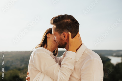 Close up portrait of faces of kissing couple. The gentleman and a girl in white shirts hugging and kissing.