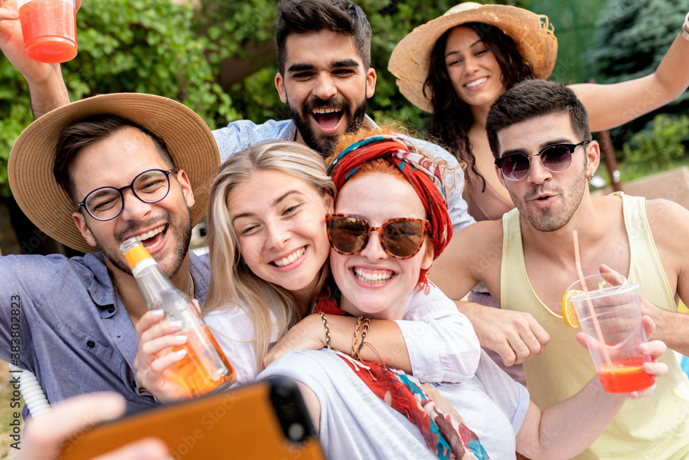 Group of young people having fun at summer vacation and enjoying a poolside party with drinks and making selfie.	