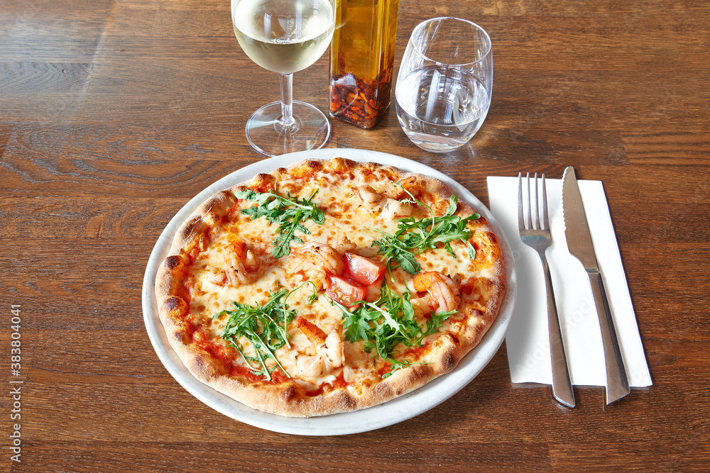 Silverware on Brown wooden table and White plate with round pizza and shrimp.