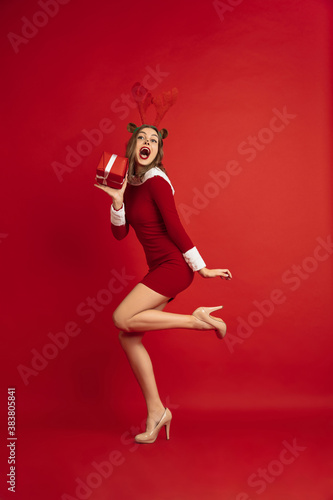 Stylish dancing with gift. Concept of Christmas, 2021 New Year's, winter mood, holidays. Copyspace for ad, postcard. Beautiful caucasian woman with long hair like Santa's Reindeer catching giftbox.
