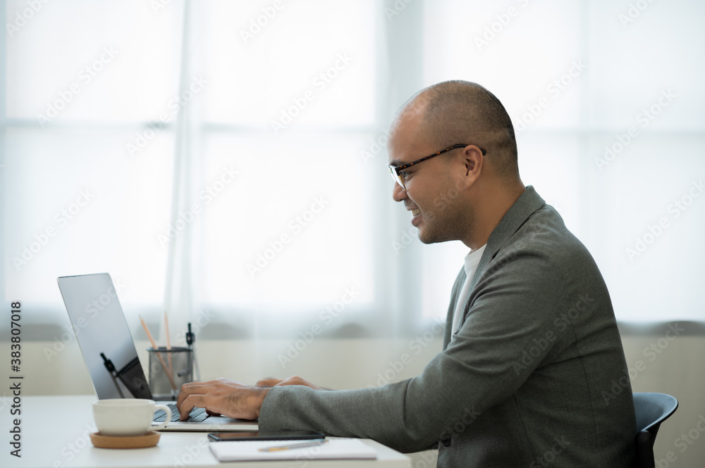 A middle-aged man around the age of 35. Working at home Work through the laptop by meeting video conference. He was wearing a grey suit and glasses. Smiling asian businessman work from home.