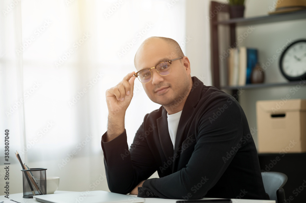 A middle-aged man around the age of 35. Working at home looking at camera. He was wearing a black suit and glasses. Smiling asian businessman work from home. A middle-aged man around the age of 35. Working at home looking at camera. He was wearing a black suit and glasses. Smiling asian businessman work from home.
