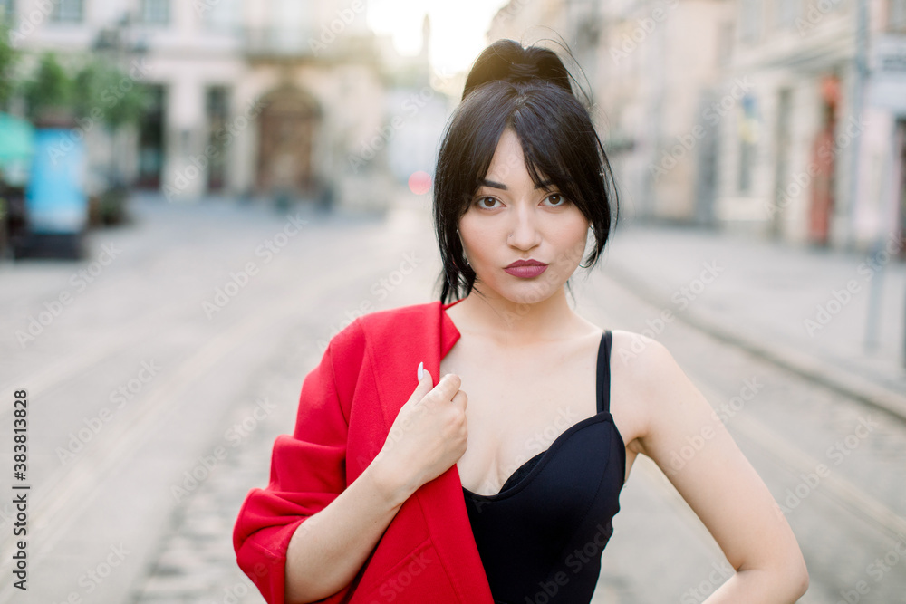 Street portrait of young sexy beautiful Asian woman, wearing stylish fashionable black top and red blazer on one shoulder, looking at camera. Female fashion concept. Copy space