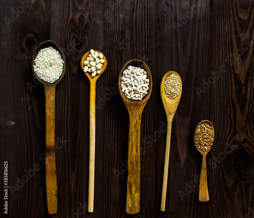 Top view of wooden spoons on which lie an assortment of different cereals on a wooden table.