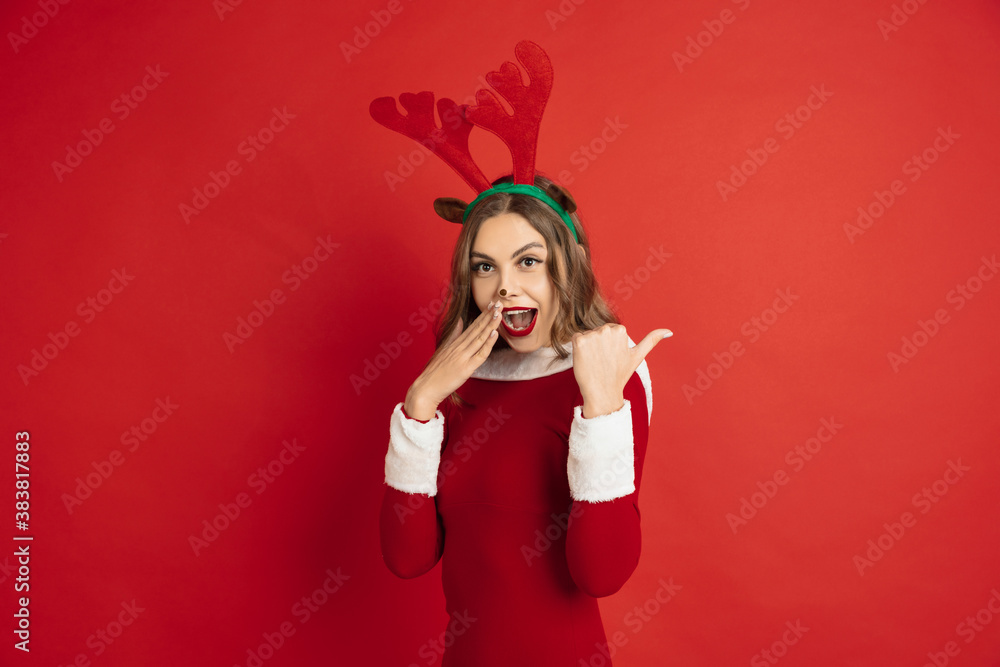 Naklejka premium Pointing. Greetingcard. Concept of Christmas, 2021 New Year's, winter mood, holidays. Copyspace for ad, postcard. Beautiful caucasian woman with long hair like Santa's Reindeer catching giftbox.