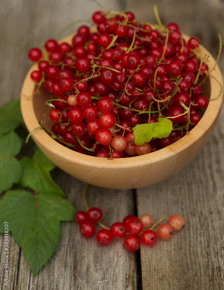 red currants and leaves in a wooden bowl against brown background red currants and leaves in a wooden bowl against brown background