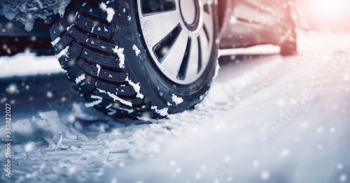 Closeup of the car tire on winter road covered with snow in snowfall in sunny day © candy1812