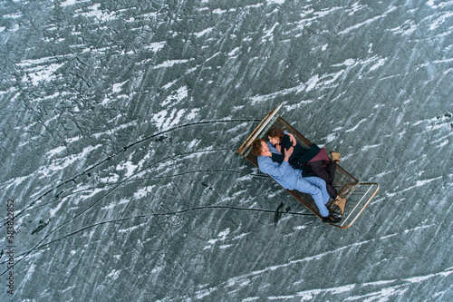 A guy and a girl in pajamas are lying on an iron bed on the ice of a frozen lake.