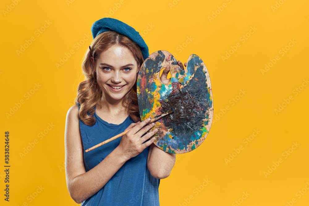 Fototapeta premium Woman with palette in blue hands takes paintbrush hobby artwork yellow background