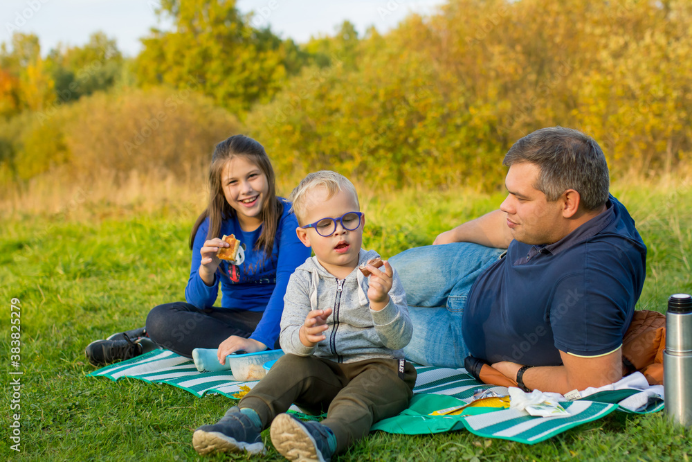 Family sitting in the Park on a picnic, Father with children, Children eating in nature.
