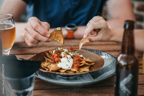 Close up of two people s hands  while eating a nacho bowl with molten cheese  sour cream and salsa