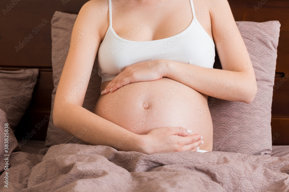 Young pretty pregnant woman, in pain, sitting on bed in bedroom, preparing to give a birth Young pretty pregnant woman, in pain, sitting on bed in bedroom, preparing to give a birth