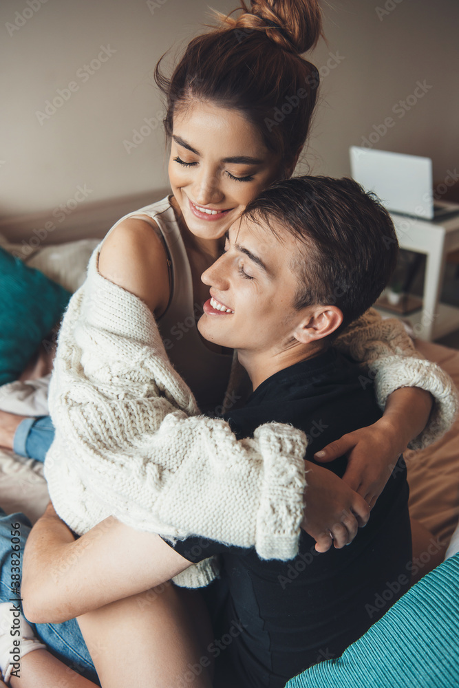 Caucasian woman embraced by her lover while playing in bed early morning in a knitted sweater smiling with closed eyes Caucasian woman embraced by her lover while playing in bed early morning in a knitted sweater smiling with closed eyes