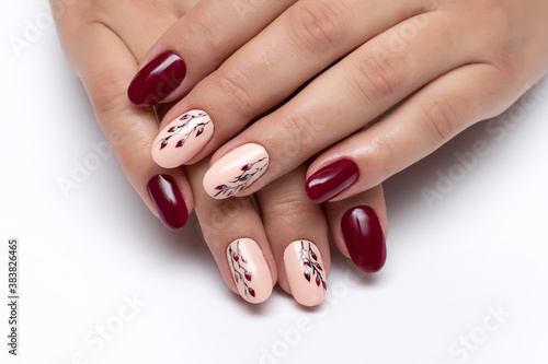 Gel burgundy, peach manicure with leaves on long oval nails close-up on a white background.