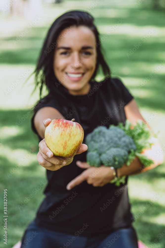 Portrait of smiling young tanned woman in the park holding an apple and a bouquet of greens with broccoli, diet, healthy eating. Soft selective focus. Portrait of smiling young tanned woman in the park holding an apple and a bouquet of greens with broccoli, diet, healthy eating. Soft selective focus.