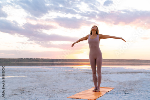 Young woman practicing yoga while doing workout on fitness mat outdoors