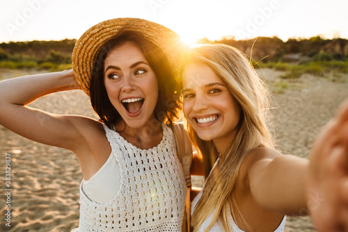 Two young caucasian women smiling and taking selfie photo on beach