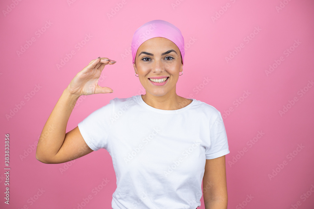 Young beautiful woman wearing pink headscarf over isolated pink background smiling and confident gesturing with hand doing small size sign with fingers looking and the camera. Measure concept. Young beautiful woman wearing pink headscarf over isolated pink background smiling and confident gesturing with hand doing small size sign with fingers looking and the camera. Measure concept.
