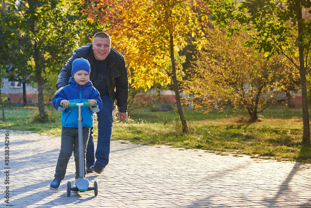 Obraz premium Dad teaches his two-year-old son to ride a scooter.