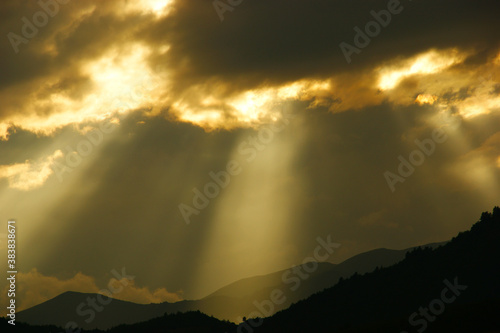 dramatic sky. Sun beams or rays breaking through the dark clouds at sunset. silhouettes of mountains and clouds at dawn © Otar