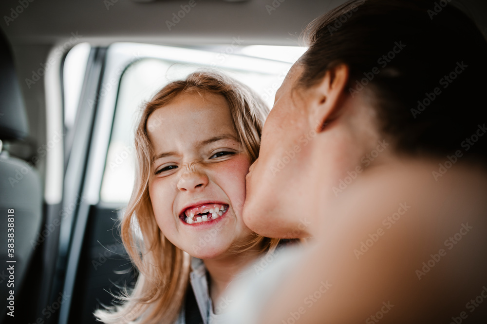 Happy daughter kissed by mother looking at camera Happy daughter kissed by mother looking at camera