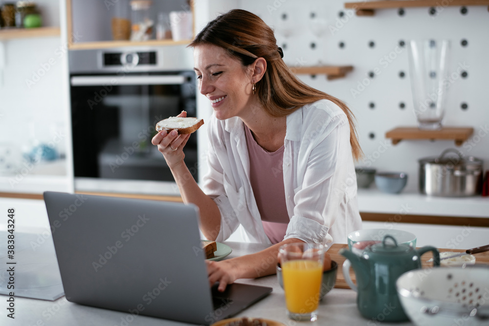 Beautiful woman eating breakfast in the kitchen. Young woman reading the news online.. Beautiful woman eating breakfast in the kitchen. Young woman reading the news online..
