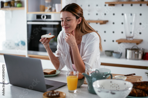 Beautiful woman eating breakfast in the kitchen. Young woman reading the news online..