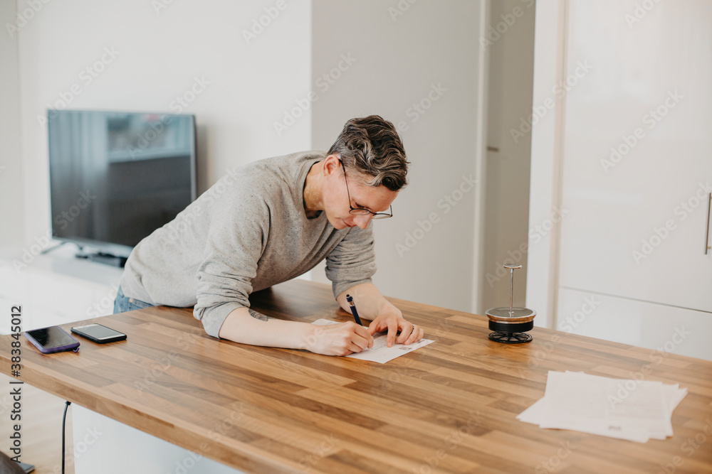 Woman writing on kitchen worktop Woman writing on kitchen worktop