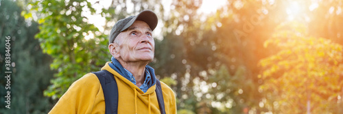 old happy male hiker with backpack looking on mountain top forest background